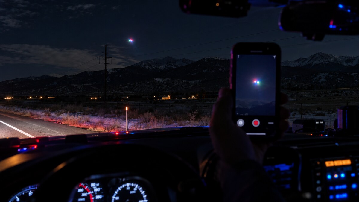 Ricostruzione editoriale di un agente che filma una luce colorata sopra le montagne del Colorado